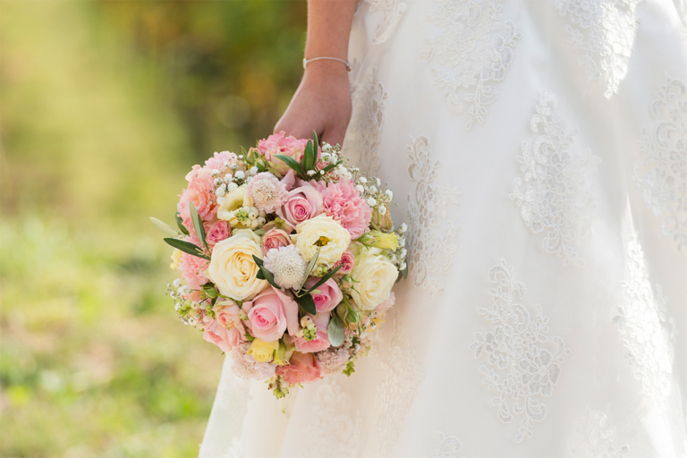Eine Braut mit weissem Kleid hält einen bunten Brautstraus in der Hand