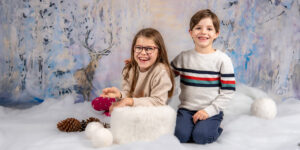Zwei Kinder sitzen auf einem verschneiten Weihnachts Hintergrund.